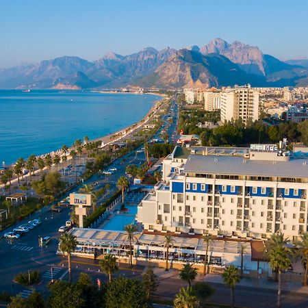 Sealife Family Resort Hotel Antalya Luaran gambar The photo depicts a scenic coastal view, featuring a beachfront area lined with palm trees. In the foreground, there is a hotel or resort with a pool and outdoor seating. The road runs parallel to the beach, with some vehicles visible. In the backgro