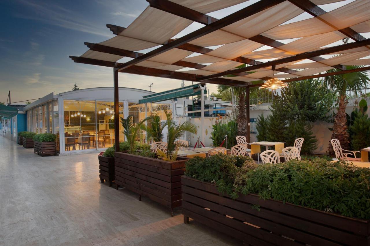 Sealife Family Resort Hotel Antalya Luaran gambar The photo depicts an outdoor space, likely a café or restaurant terrace. It features a wooden structure with a grid-like canopy that provides shade, and several white chairs with decorative designs are arranged around small tables. There are large pl