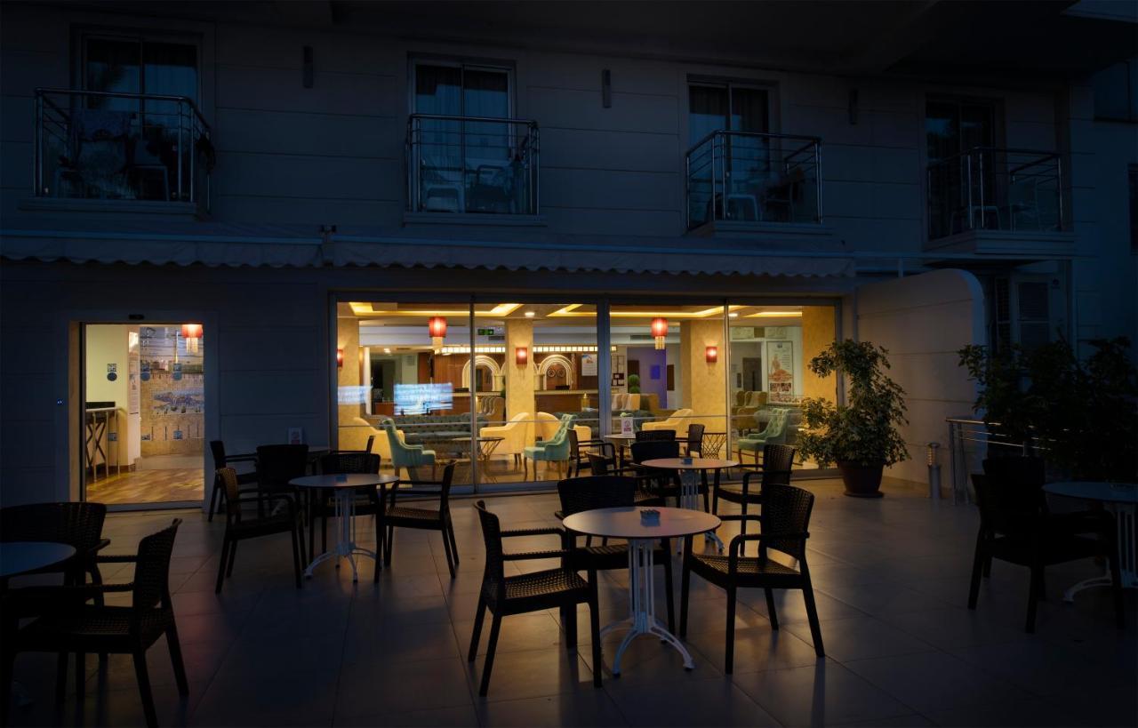 Sealife Family Resort Hotel Antalya Luaran gambar The photo depicts an outdoor seating area of a café or restaurant. In the foreground, there are several black chairs and a small round table. In the background, through large windows, you can see the interior of the establishment, which is warmly lit