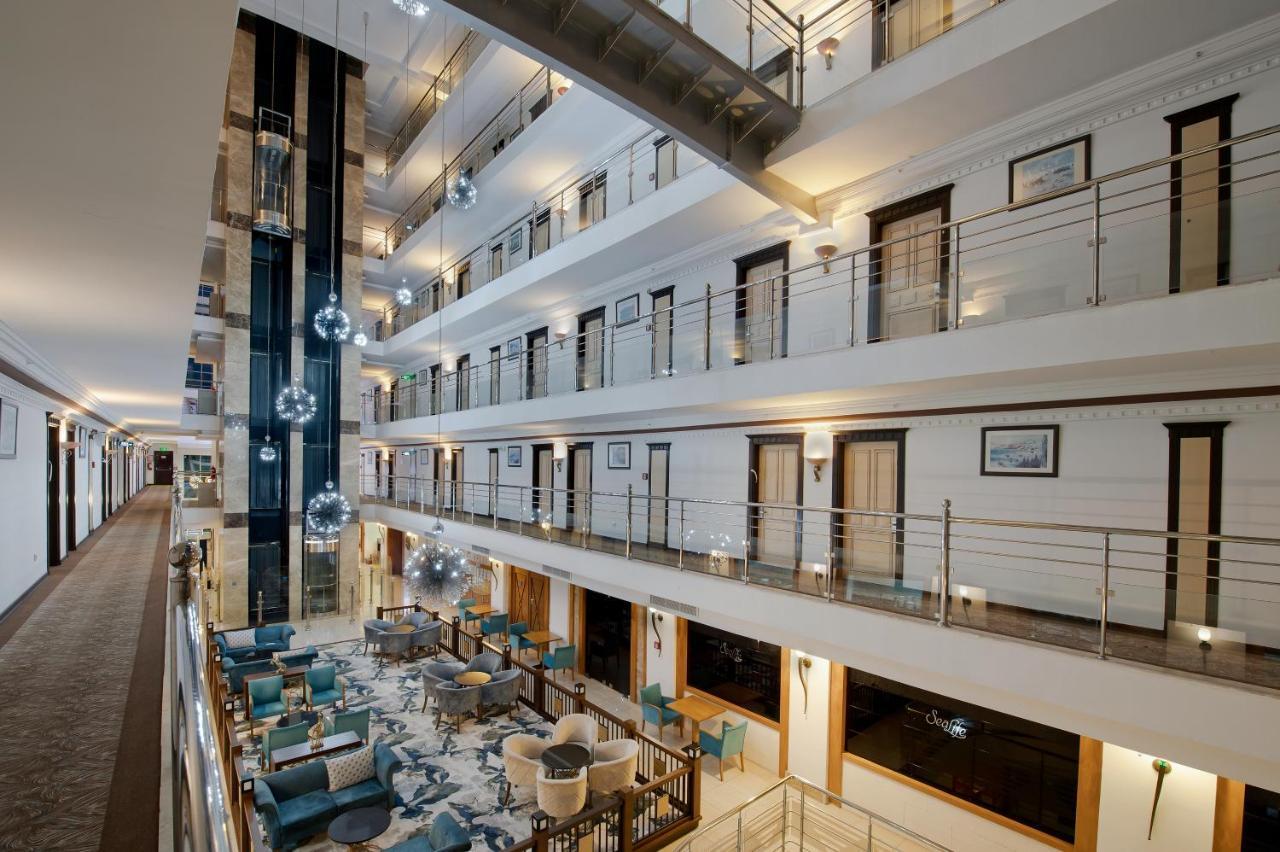 Sealife Family Resort Hotel Antalya Luaran gambar The photo shows the interior of a modern hotel or building featuring a multi-level atrium. There are several floors overlooking the central area, with glass railings providing a view of the spaces below. The decor includes stylish seating areas with 