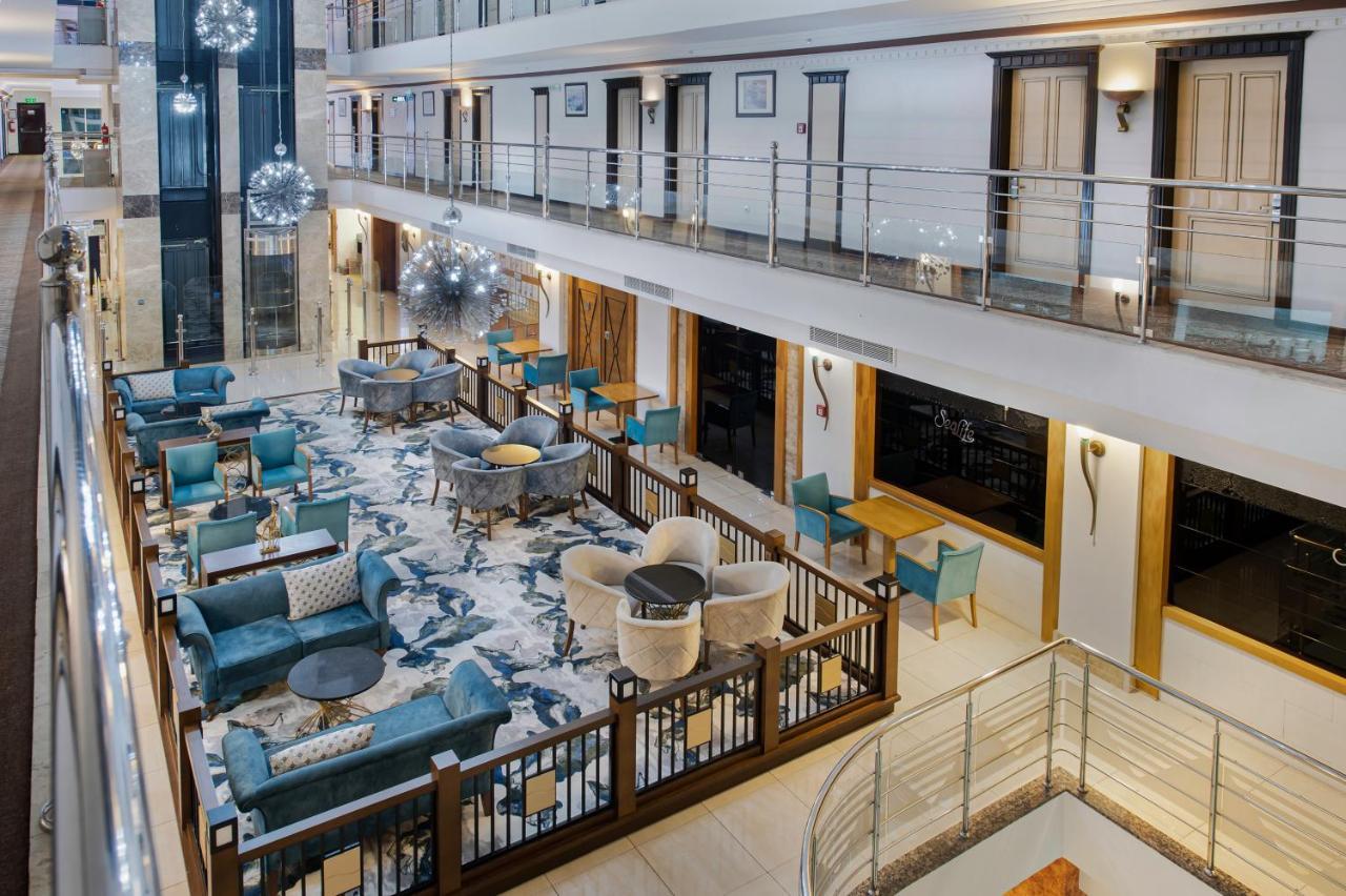 Sealife Family Resort Hotel Antalya Luaran gambar The photo shows the interior of a modern hotel lobby or lounge area. There are multiple seating arrangements with stylish teal chairs and cream-colored sofas set around tables. The floor features a large, decorative rug, and the walls have elegant fi