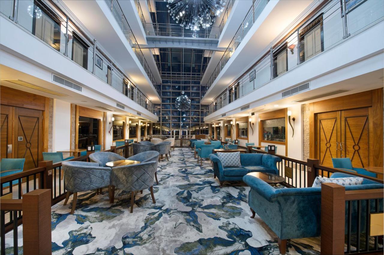 Sealife Family Resort Hotel Antalya Luaran gambar The photo shows a spacious and elegantly designed hotel lobby. There are two levels with balconies overlooking the main area. The lobby features plush, stylish seating arranged around small tables. The floor is decorated with a colorful, abstract car