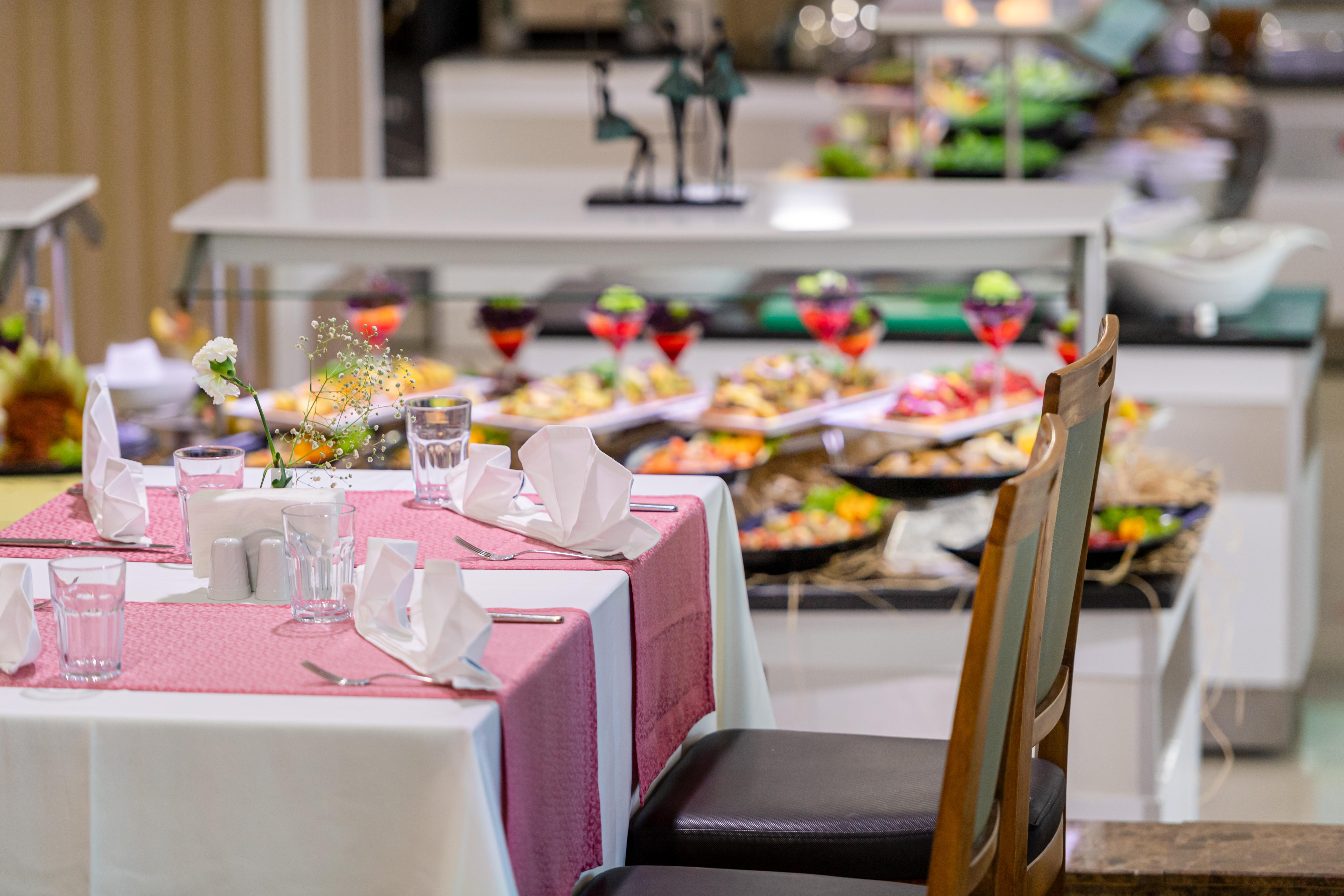 Sealife Family Resort Hotel Antalya Luaran gambar The photo features a dining area of a buffet restaurant. In the foreground, there's a neatly set table with a pink tablecloth, white napkins, and glasses. In the background, a variety of dishes is displayed on a buffet table, showcasing an assortment