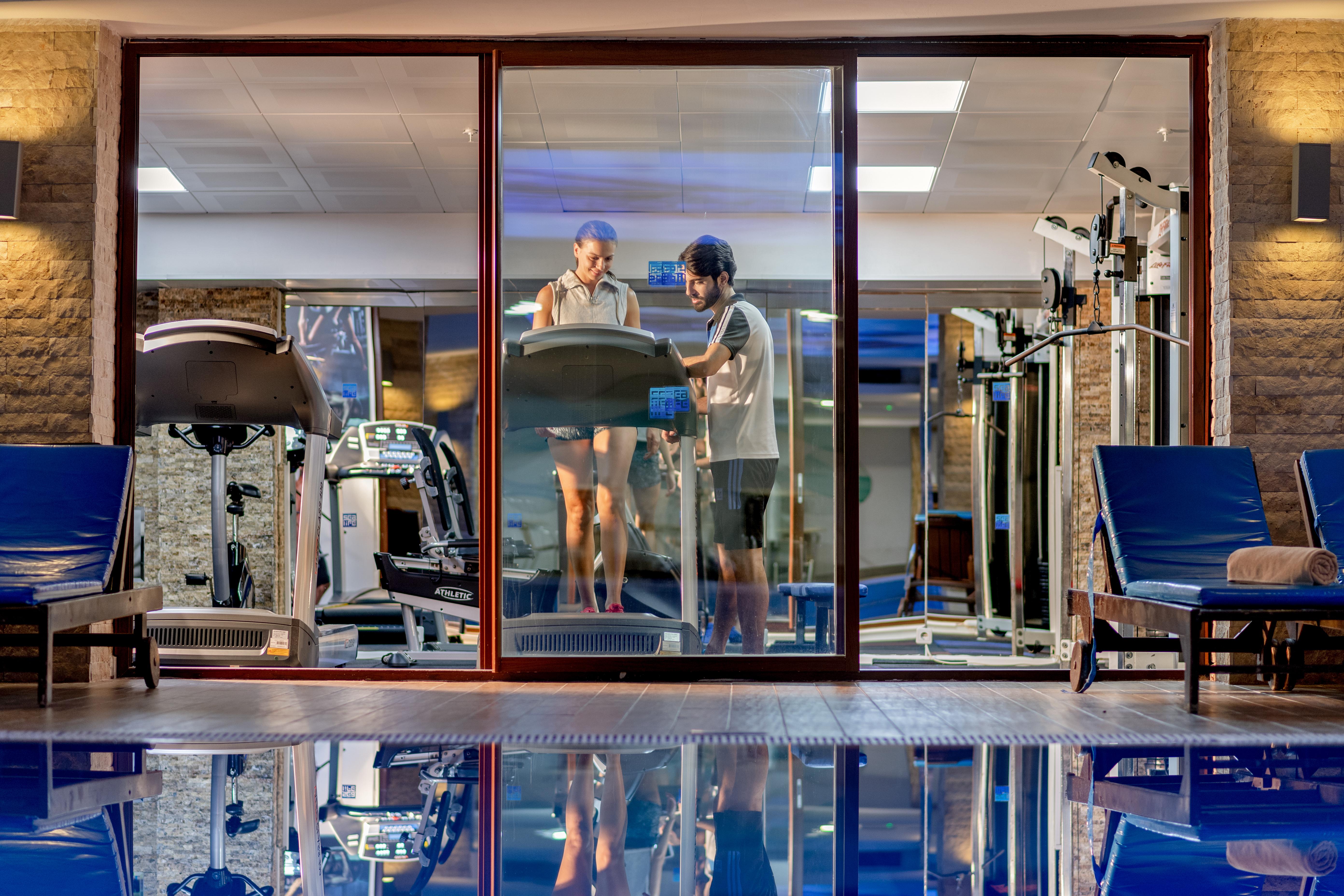Sealife Family Resort Hotel Antalya Luaran gambar The photo shows a modern gym area viewed through a large glass window. Inside the gym, there are two individuals, one on a treadmill and the other standing beside it, possibly offering guidance or support. The gym is well-equipped, featuring various 