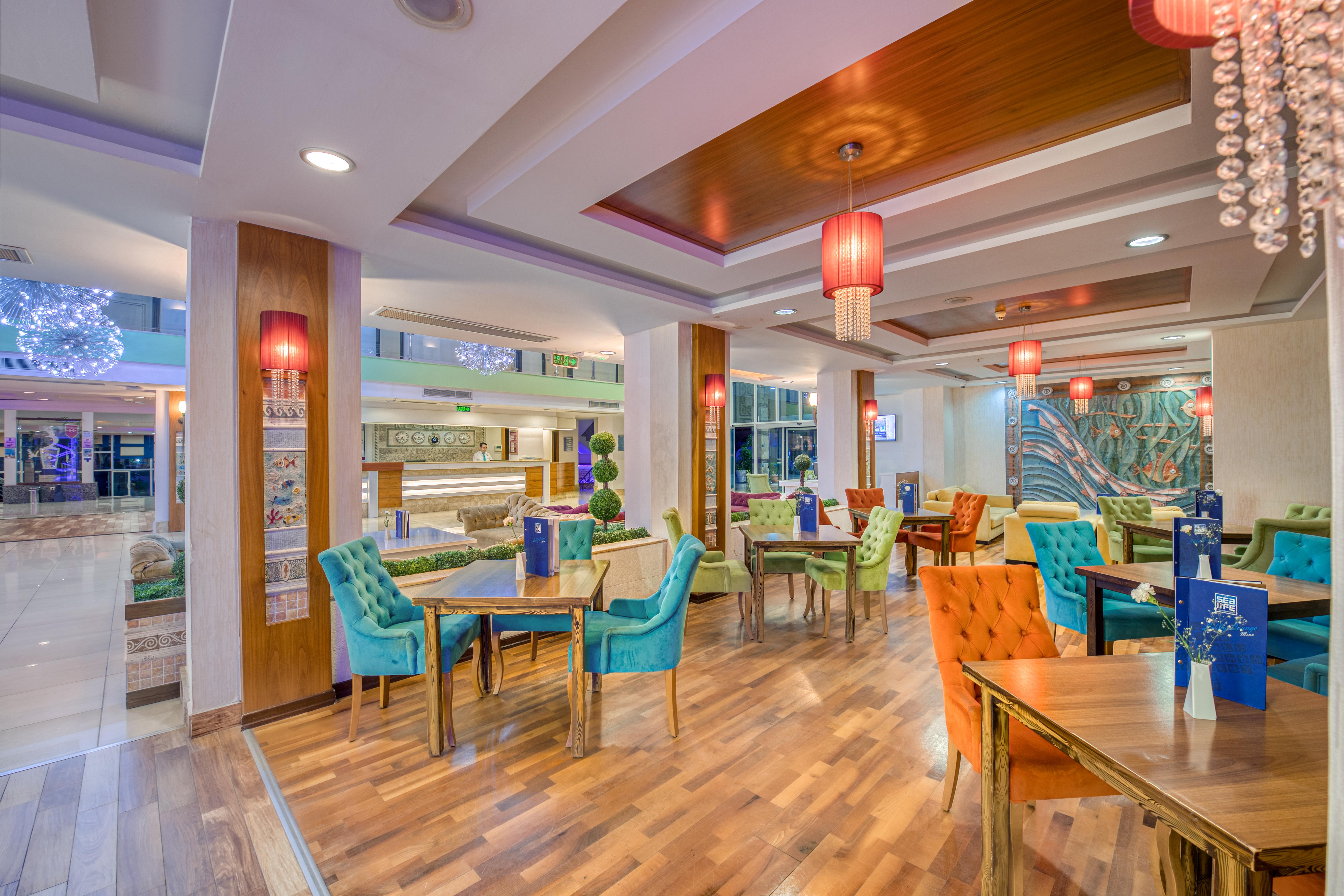 Sealife Family Resort Hotel Antalya Luaran gambar The photo depicts a vibrant and modern restaurant interior. The space features multiple dining tables, each adorned with blue menus. The chairs are brightly colored, in shades of teal, orange, and other hues, adding a playful touch to the decor. The 