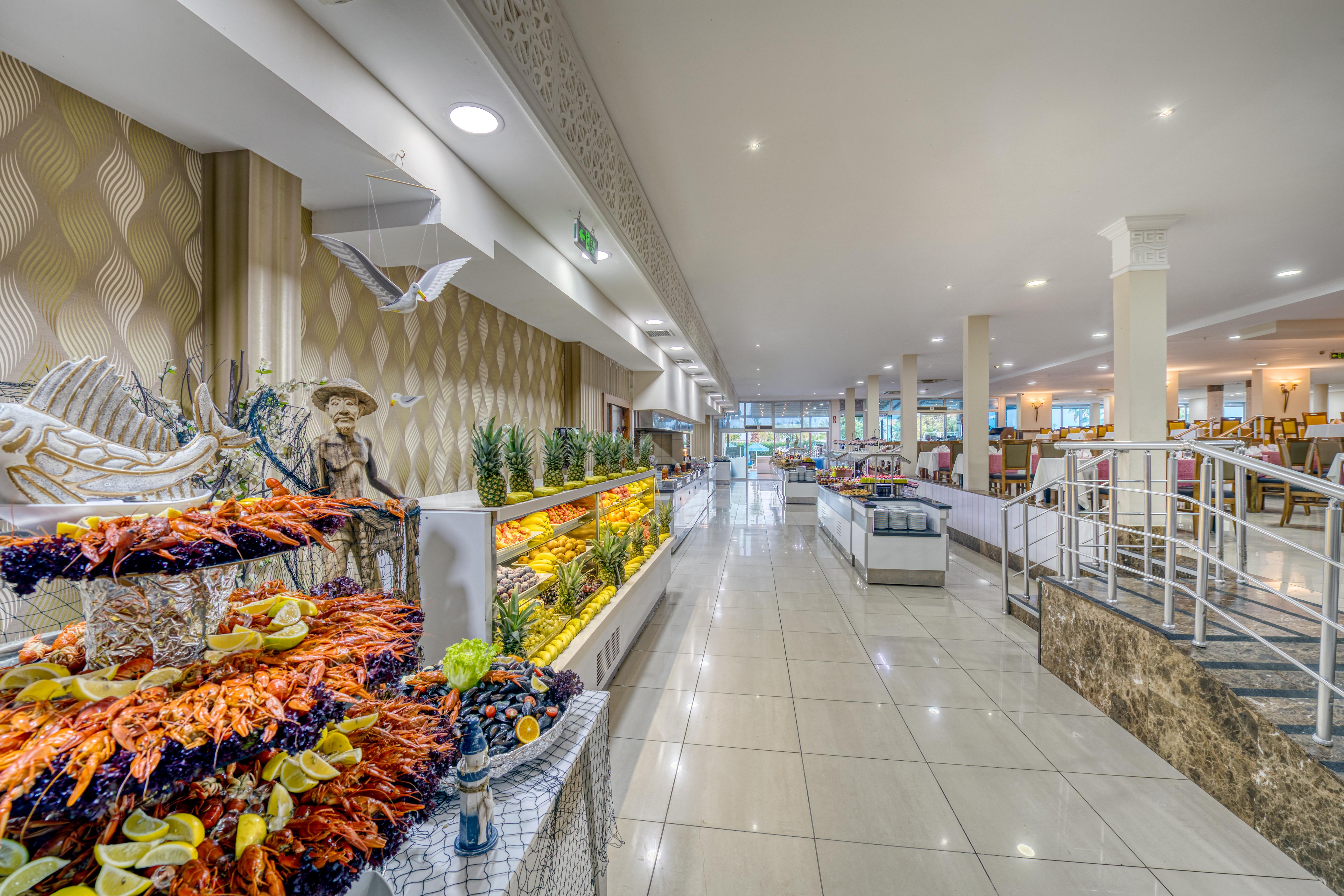 Sealife Family Resort Hotel Antalya Luaran gambar The photo shows the interior of a spacious dining area, likely in a restaurant or buffet. The space features a long corridor with glossy tiled floors and bright, well-distributed lighting. On one side, there are decorative displays of seafood, includ