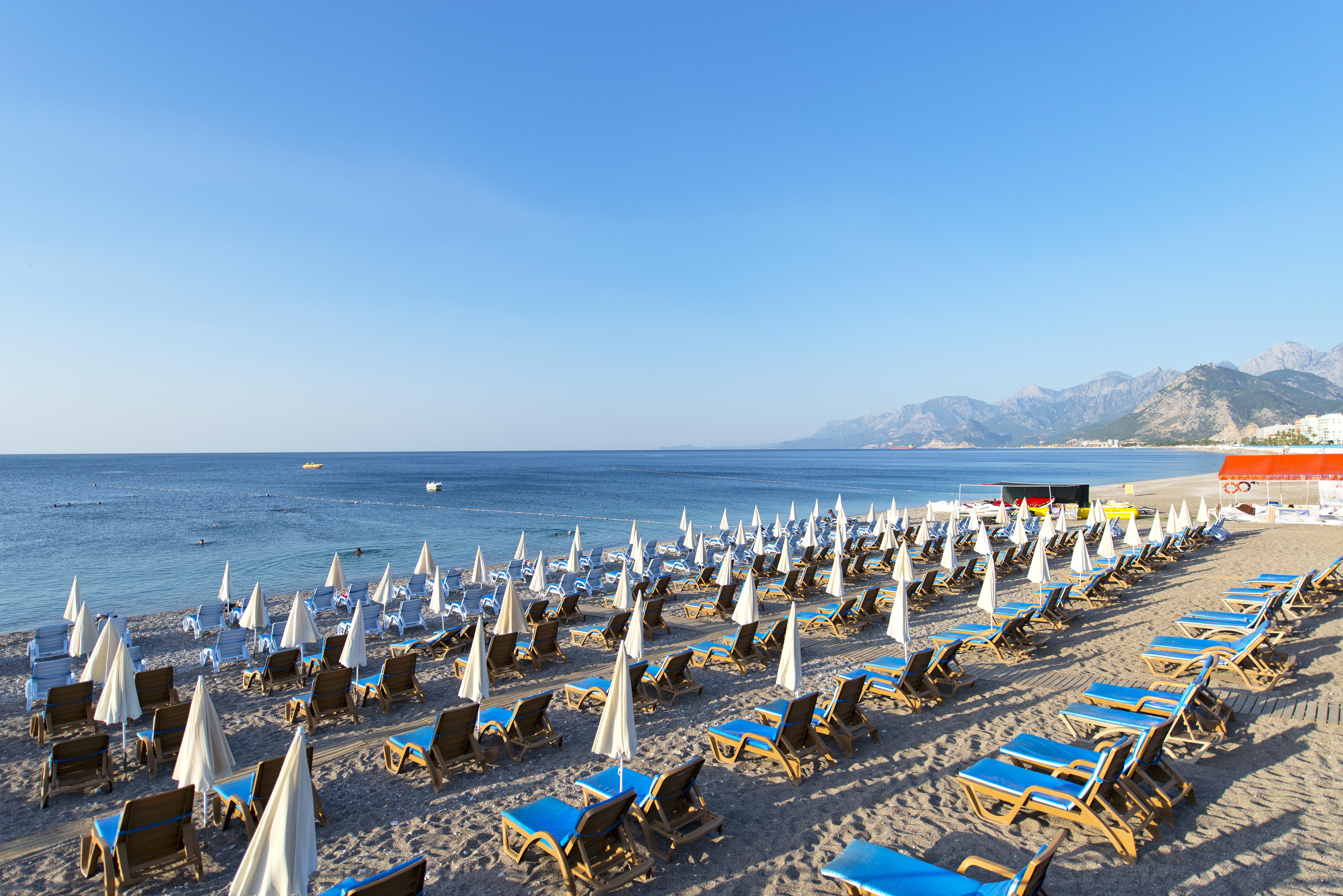 Sealife Family Resort Hotel Antalya Luaran gambar The photo depicts a beach scene with numerous sun loungers arranged in rows on the sand, each equipped with white umbrellas. The loungers are primarily blue, creating a vibrant contrast against the sandy beach. In the background, gentle waves can be 