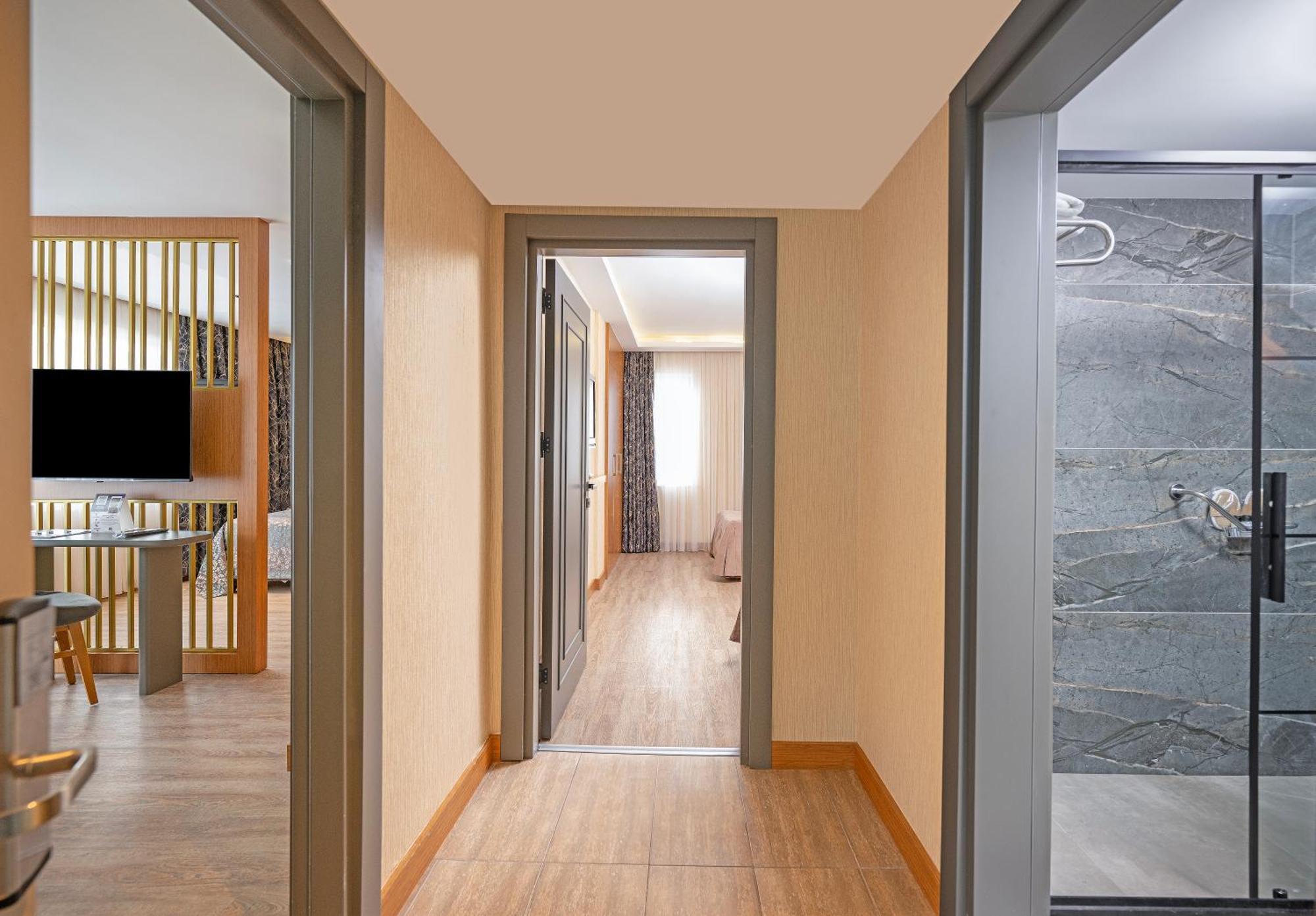 Sealife Family Resort Hotel Antalya Bilik gambar The image shows a hallway with a few separate rooms visible. On the left side, there's a view of a modern living area with a television and some furniture. At the end of the hallway, light is coming from a window in another room, indicating it may be