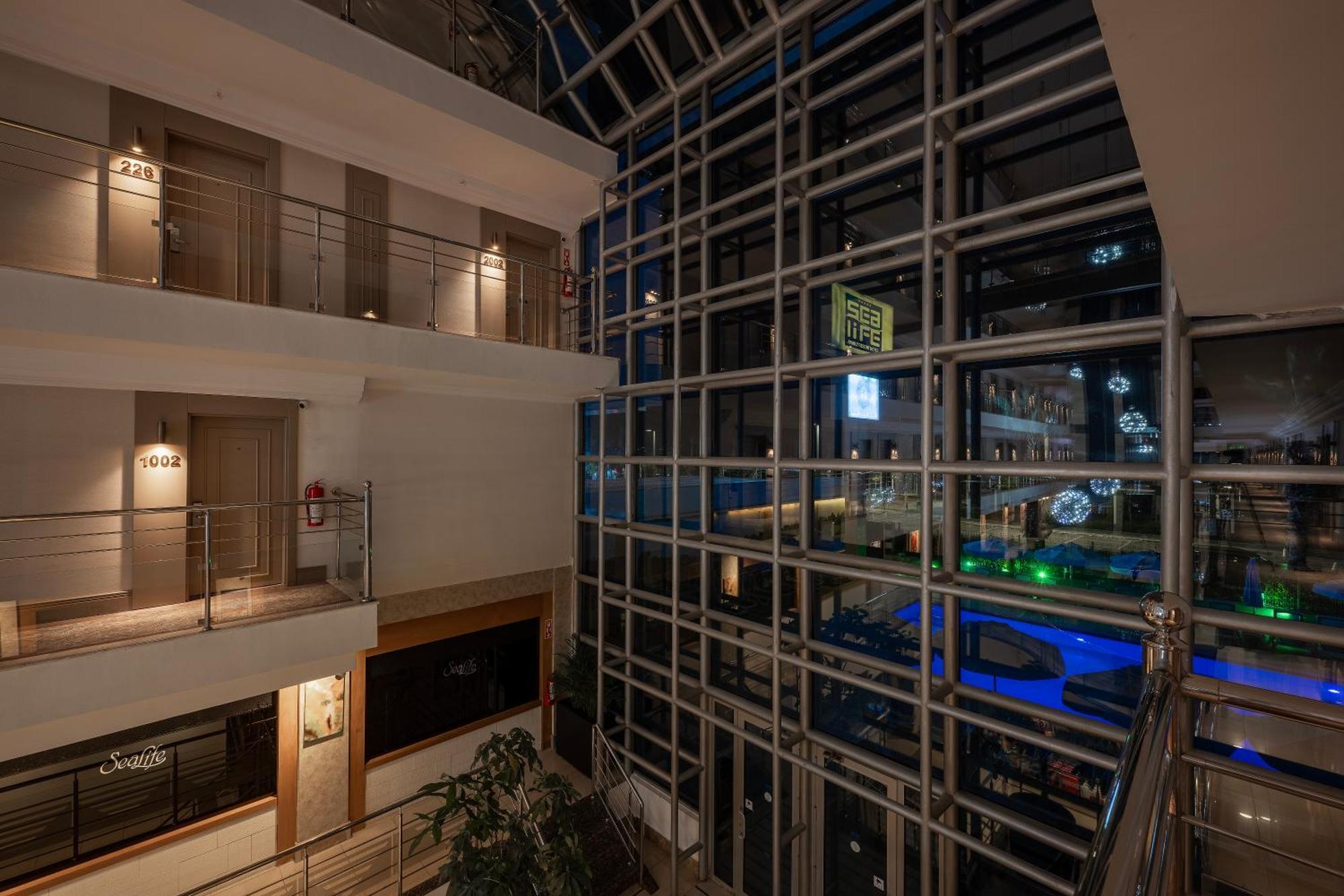 Sealife Family Resort Hotel Antalya Luaran gambar The photo shows an interior view of a modern building at night. There's a glass façade that allows for a view of the outside, which appears to be illuminated with various lights. Inside, there are several levels with walkways and balconies. The desig