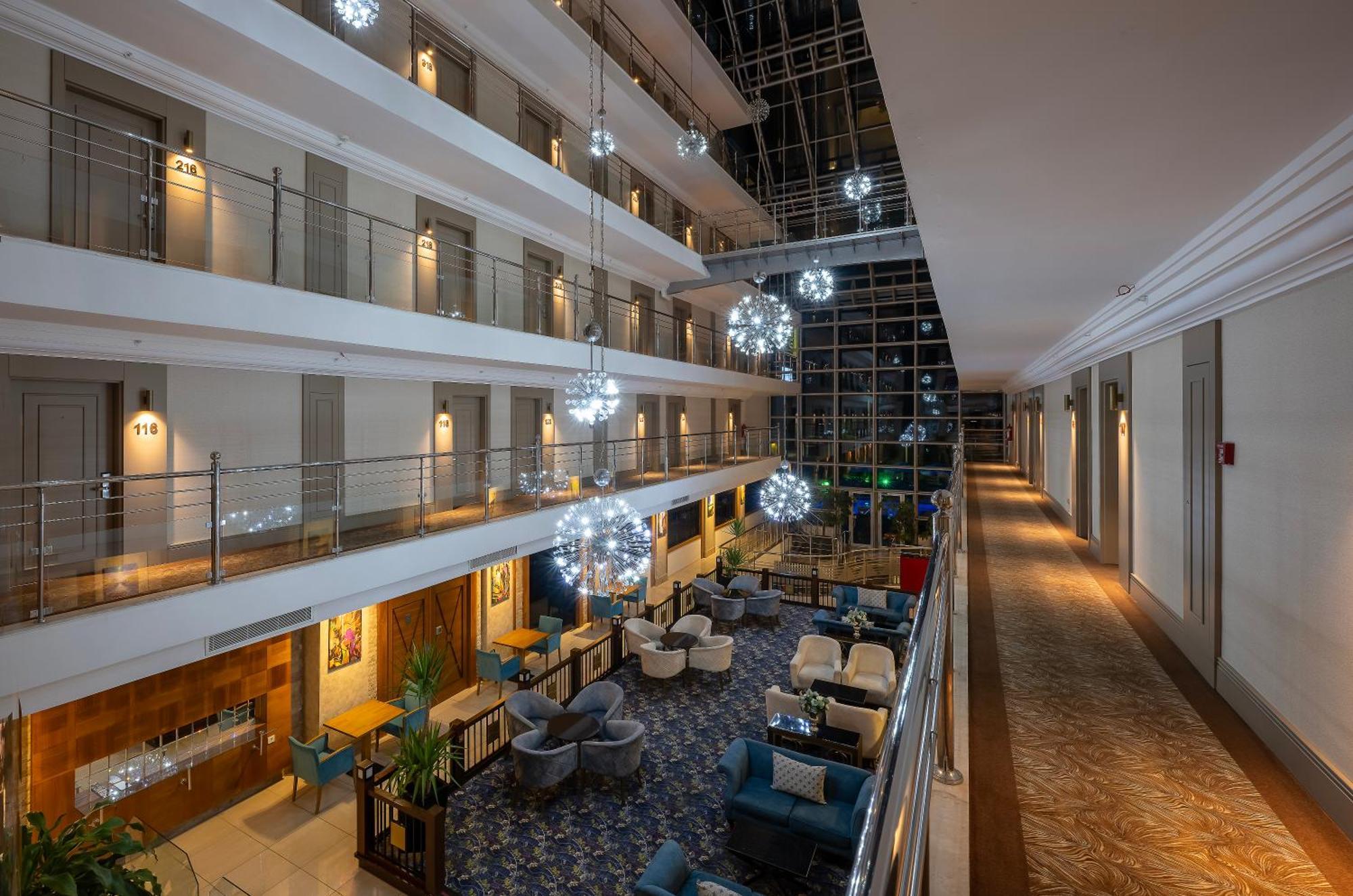 Sealife Family Resort Hotel Antalya Luaran gambar The image shows the interior of a hotel lobby or atrium. It features multiple levels with balconies overlooking a central area. The design includes elegant lighting fixtures that resemble decorative spheres, hanging from the ceiling. The floor is ado
